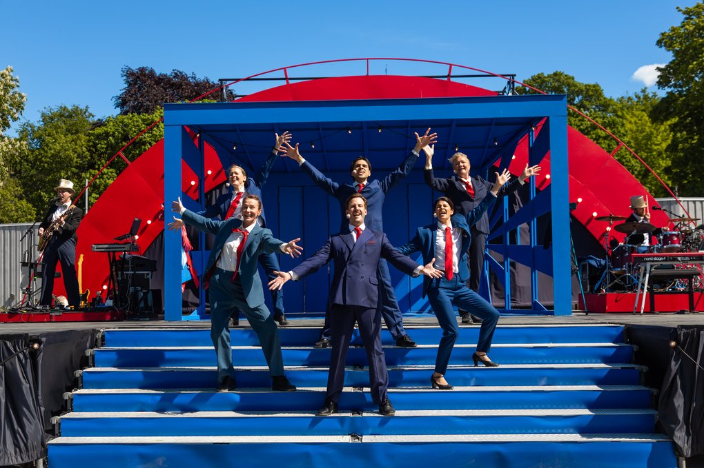 Actors in suits with red ties flamboyantly posing on a set of stairs